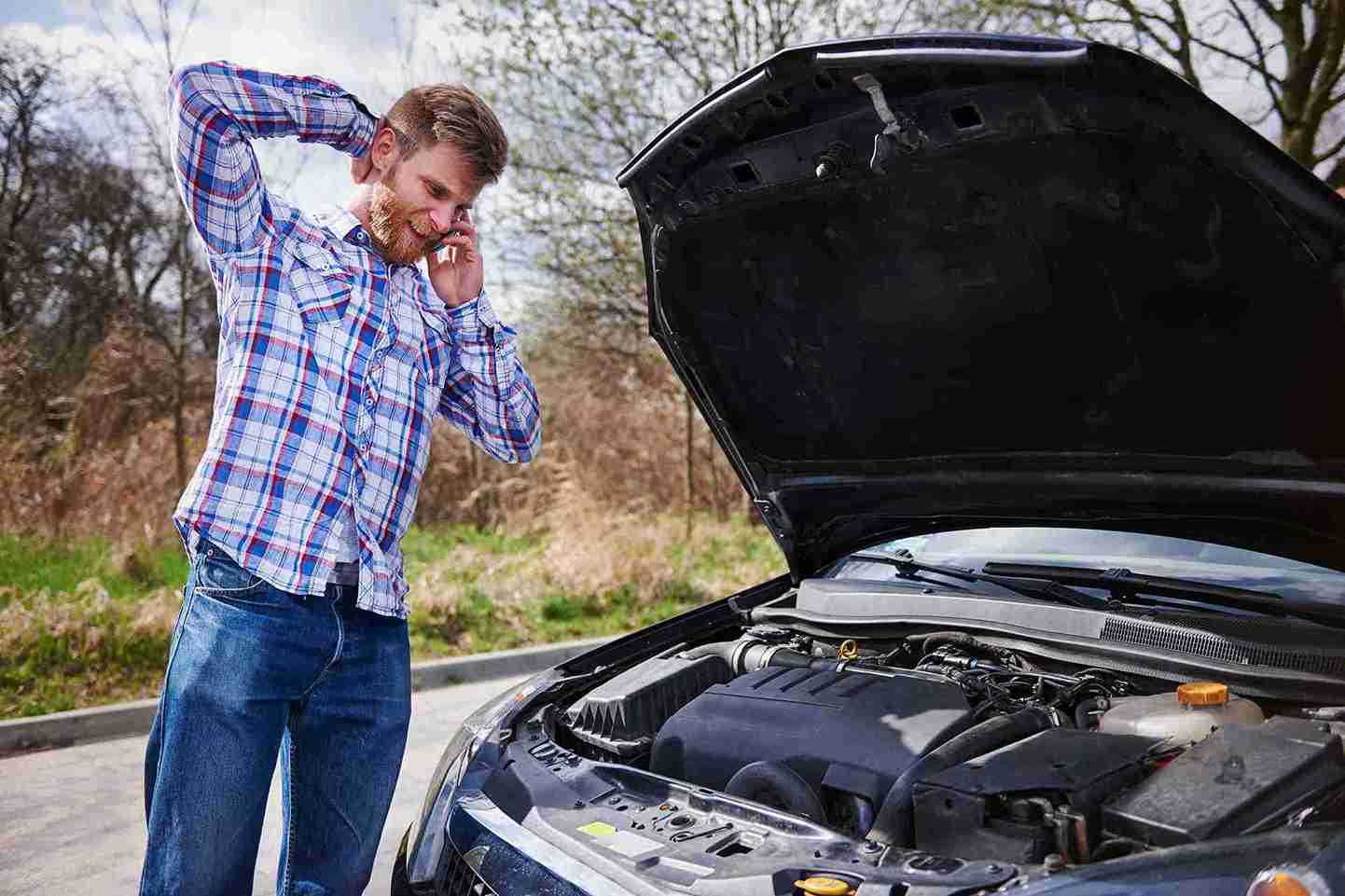 Driver on phone with car hood up deciding when to call roadside assistance in DeSoto TX